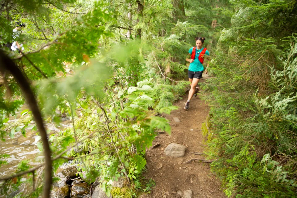 A woman trail running down a path in the summer.