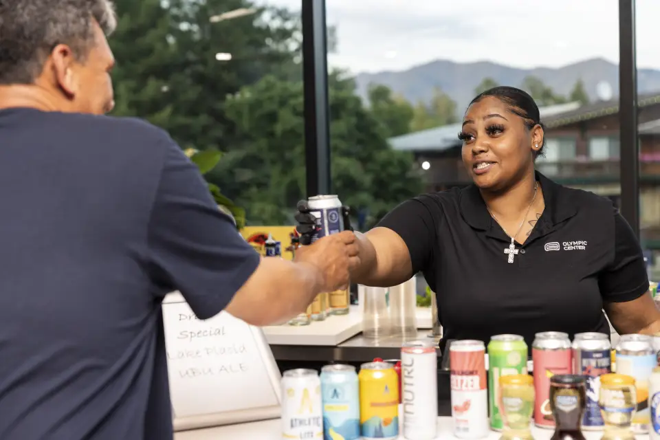 A woman bartender hands a man a drink.