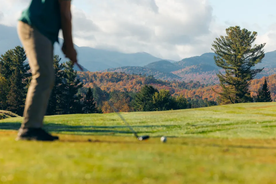 A person teeing up on the green with fall foliage in the background.