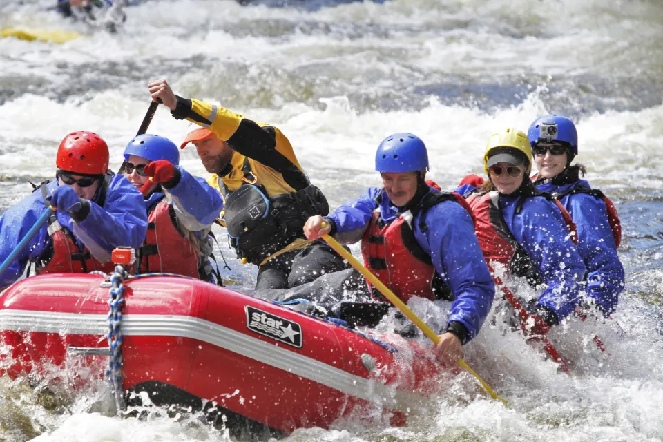 A group  of people paddle on a white water rafting trip. 
