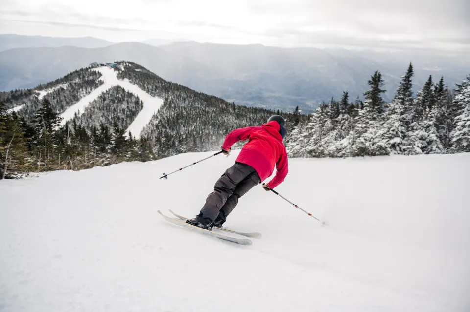 A man in a red jacket goes skiing. 