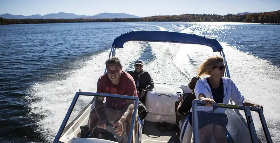 Four adults ride a motorboat on a blue lake with mountains in the distance.