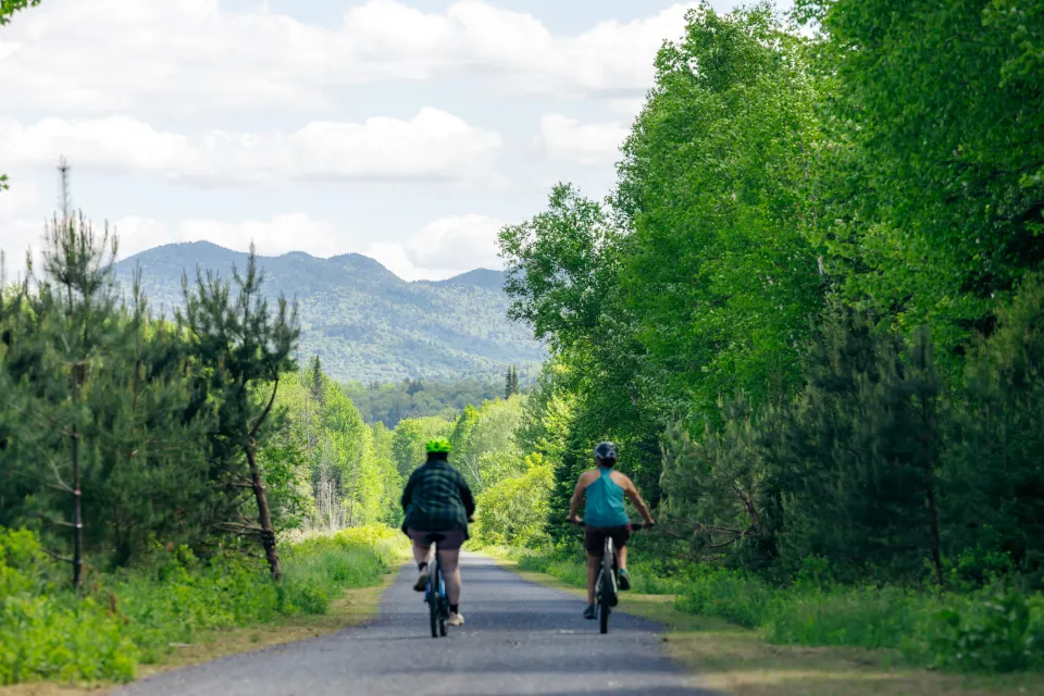 Two women ride bicycles on a backcountry path. 