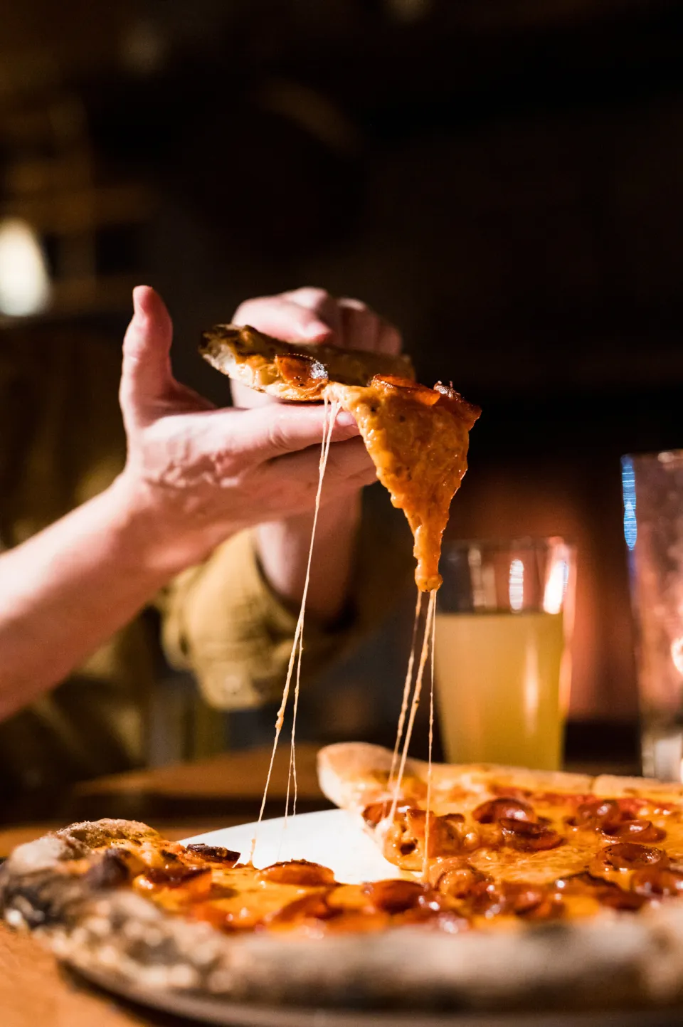 A person pulling a cheesy slice of pizza from a tray.