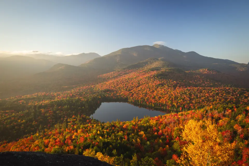 A fall mountain range covered in reds and yellows with a lake in the middle.