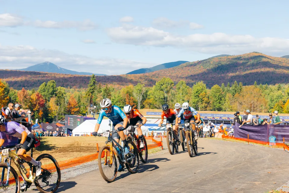 A group of cyclists race on a fall track.