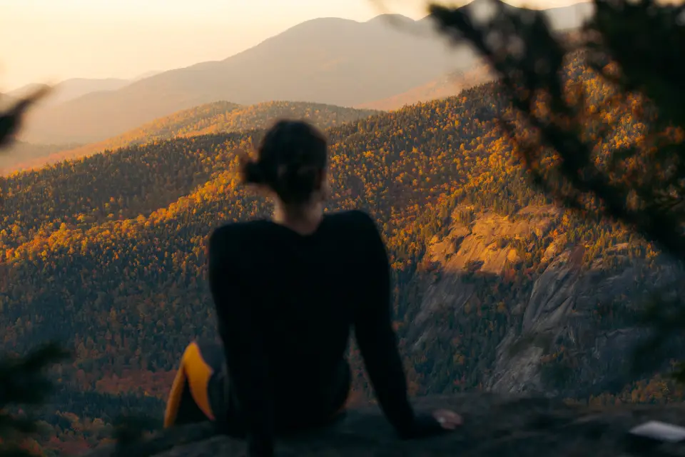 A woman sitting at the summit of a fall hike.