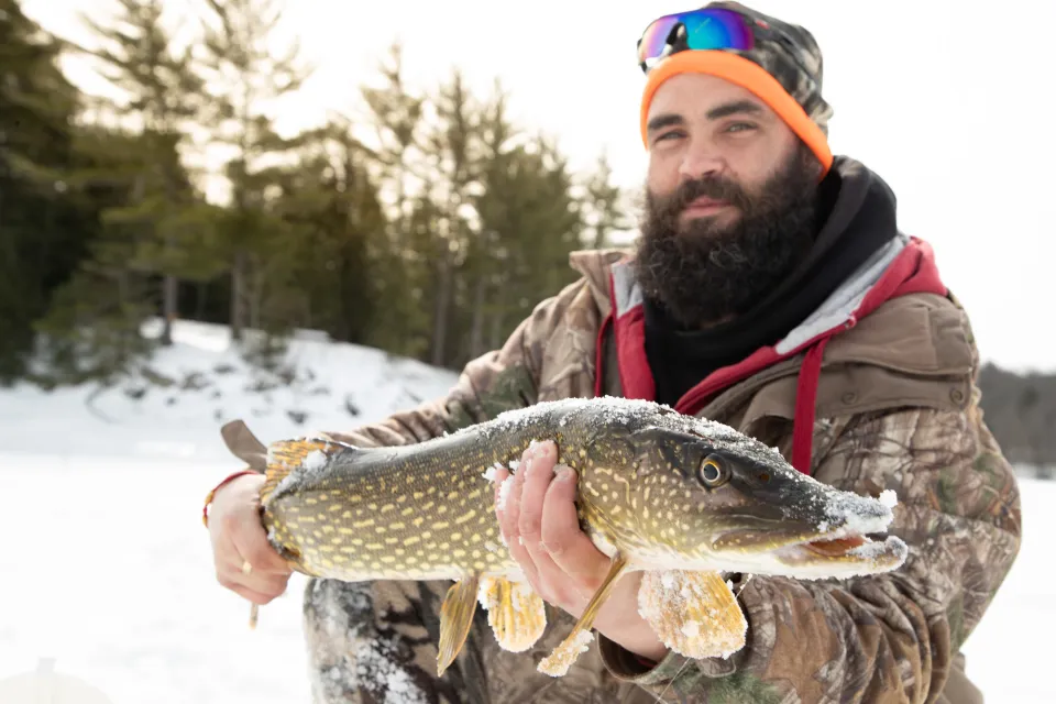 A man holds up a northern pike he caught ice fishing