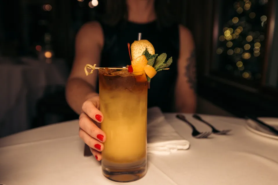 woman's hand with red  painted fingernails holds glass with yellow fruity cocktail