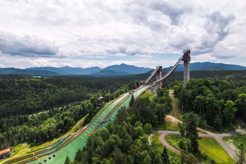 Two olympic ski jumps stand above the trees in summer. 
