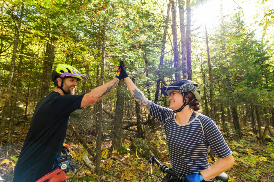 Two mountain bikers wearing biking gear stand on bikes high-fiving each other