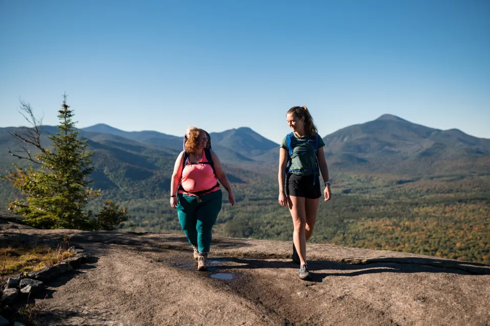 Two women hiking on a rocky mountain summit.