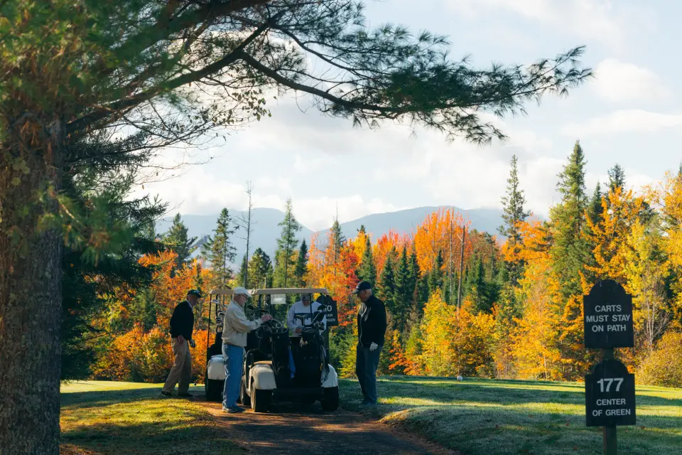 Three older men play golf in fall surrounded by foliage.