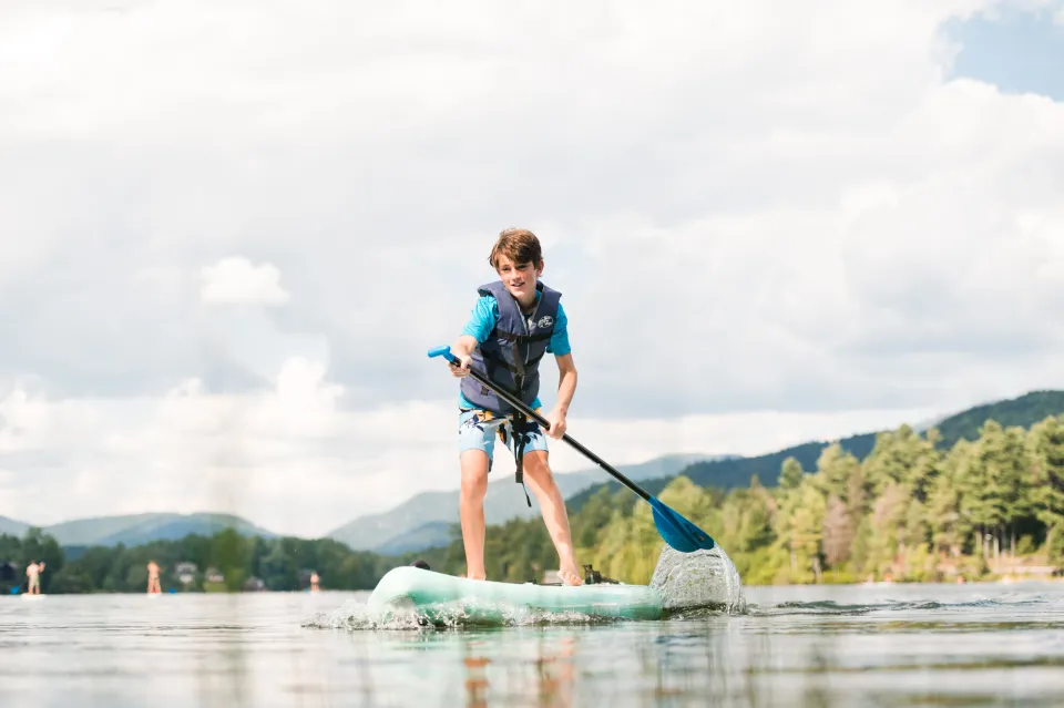 A young boy wears a life jacket while paddling on a stand up paddle board.