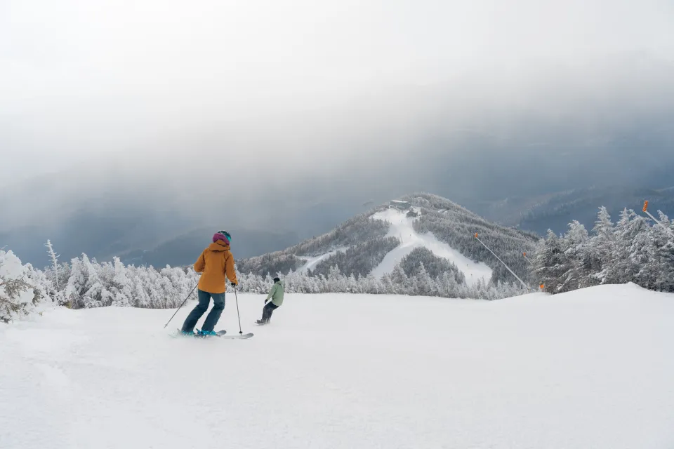 Two people ski down an empty summit on a ski mountain in winter. 