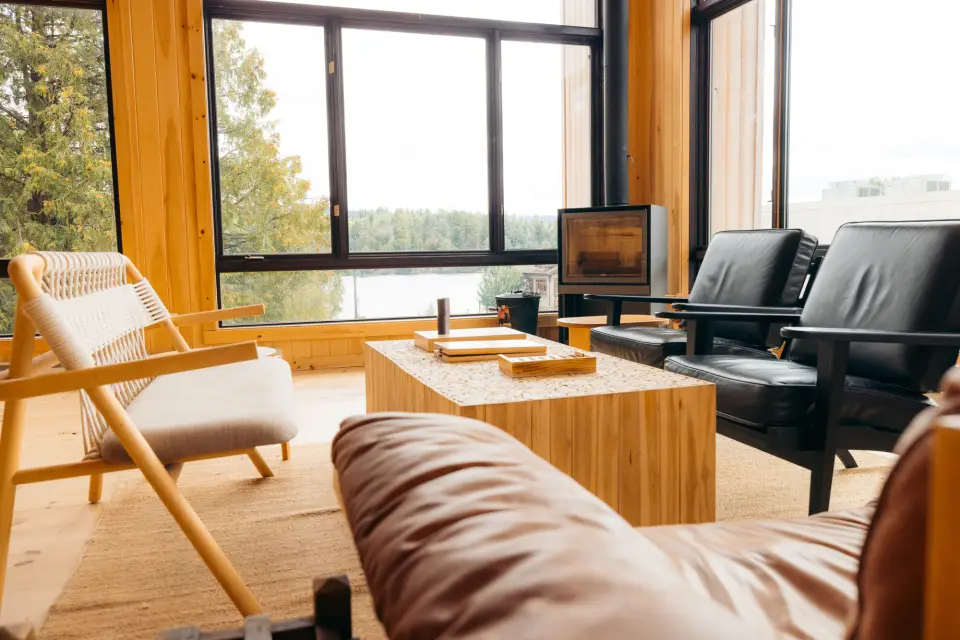 A hotel lounge features large windows, a woodstove in the corner, and light-colored Scandinavian chairs and sofas.