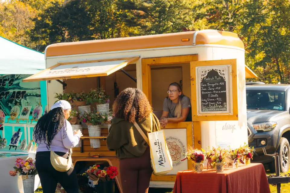 Two women buy flowers from a flower truck.