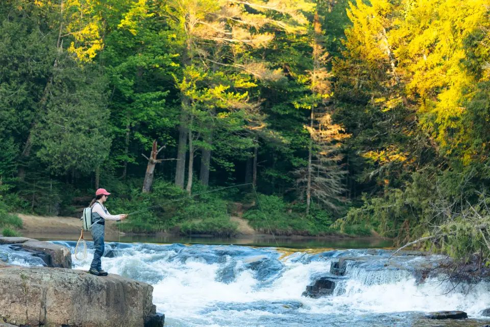 A women fly fishing on a rock by a fast moving river