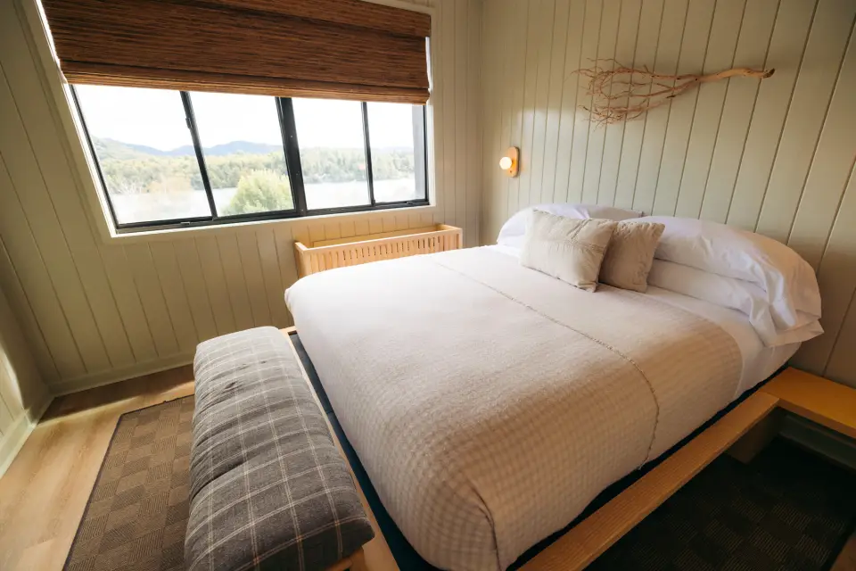 Part of a hotel room, showing a queen-size bed with plush blankets, an upholstered bench, and bead-board paneling.