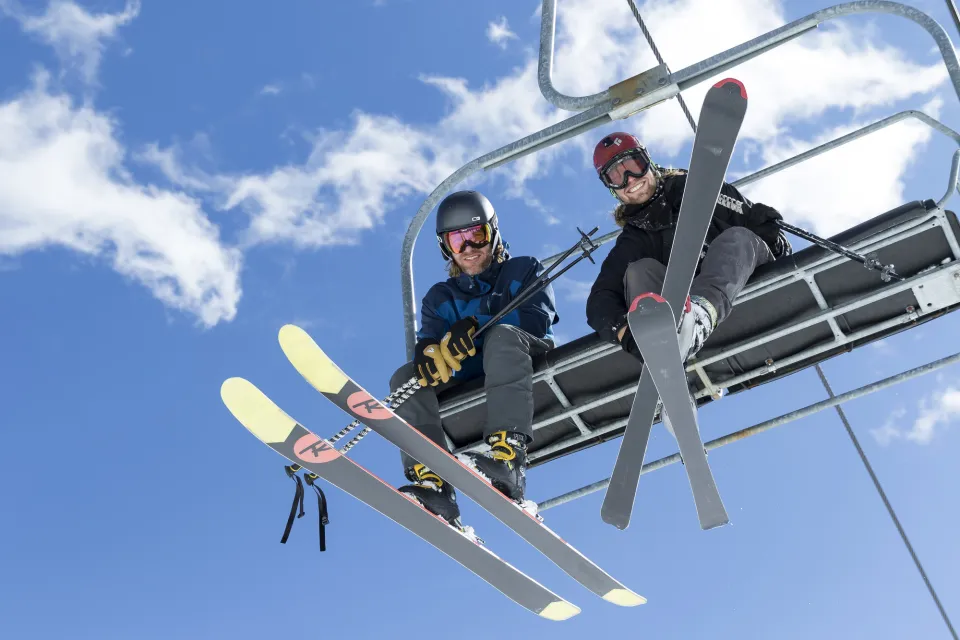 Two men smile while riding a chairlift in skis. 