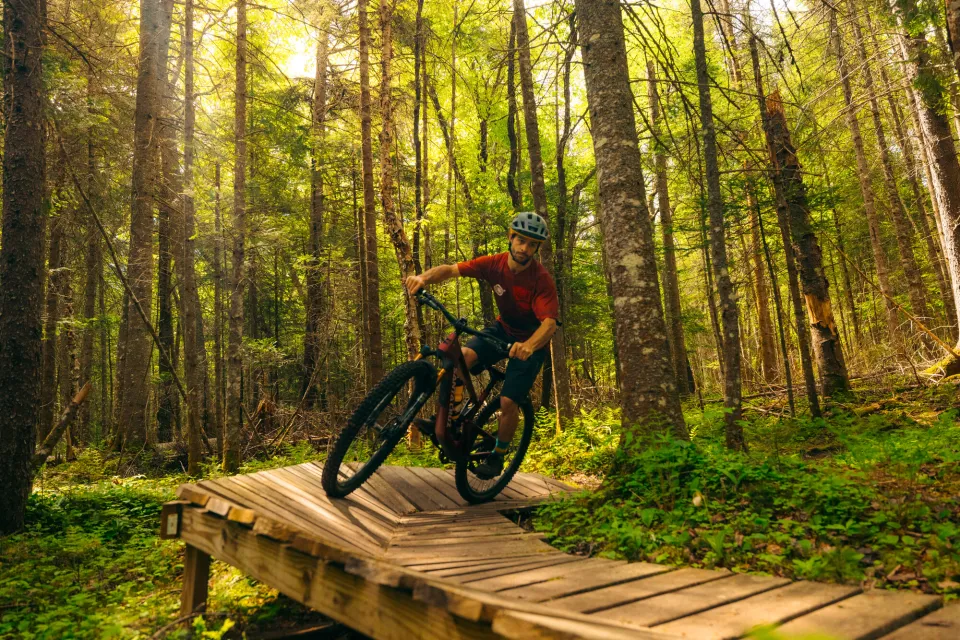 Mountain biker in red rides over wooden boardwalk on forest trail