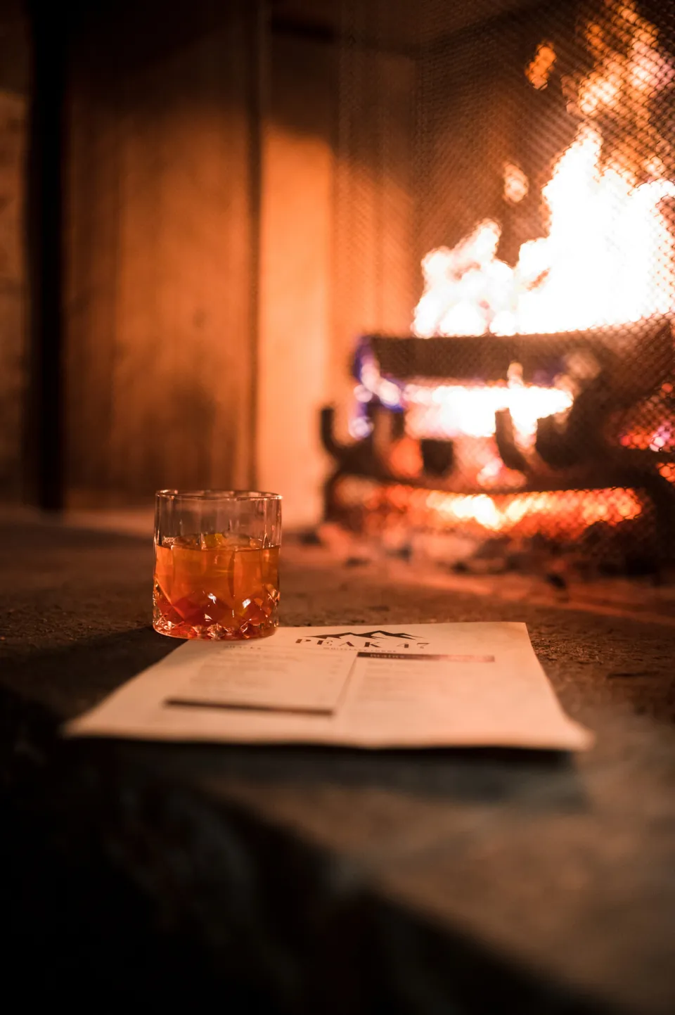 An alcoholic beverage sitting in front of a cozy fireplace.