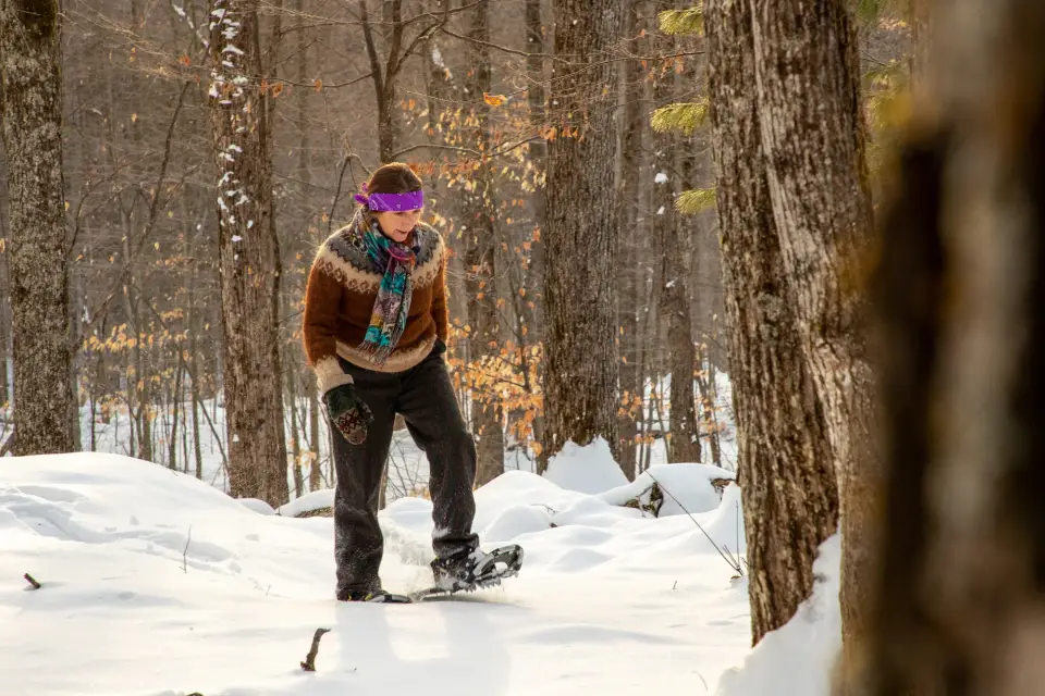 A woman in a brown jacket snowshoes in the winter.