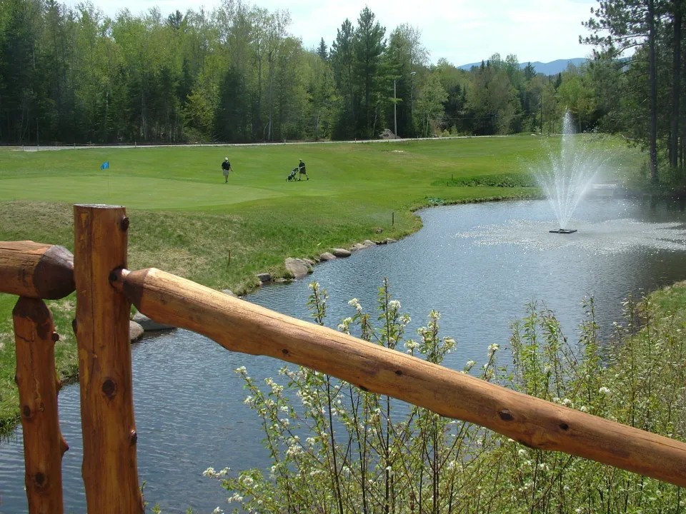 A rustic railing on a small bridge over a pond at a golf course.