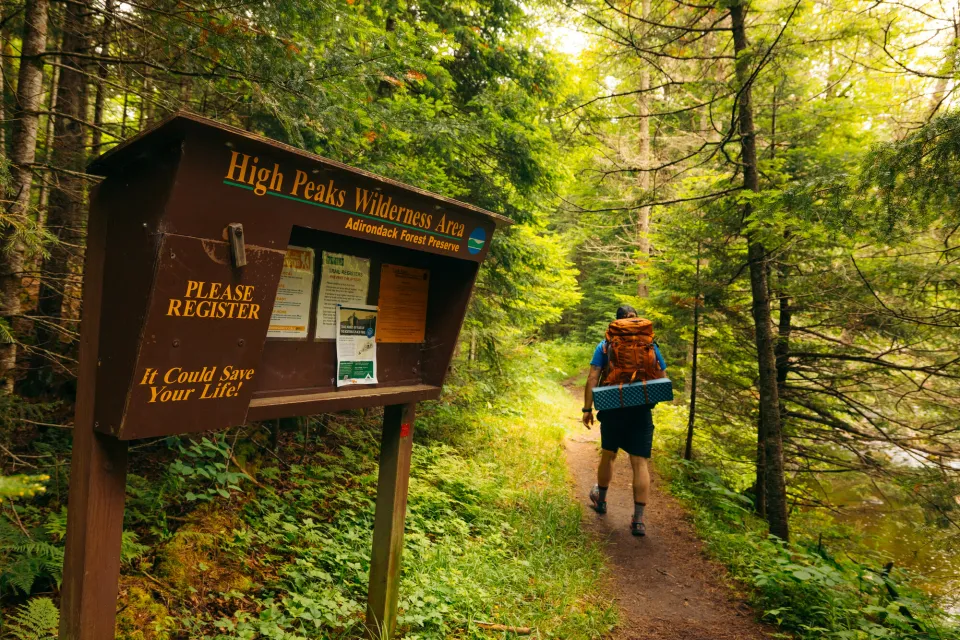 A hiker walking past a trail register. 
